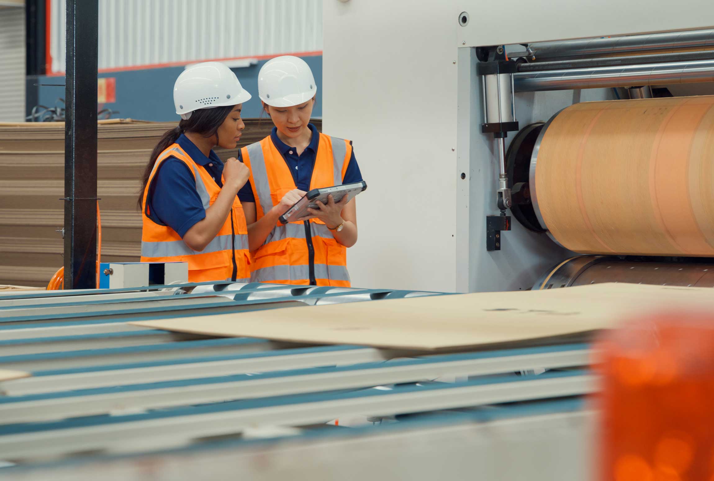 Two women looking at a tablet in a factory manufacturing cardboard boxes.