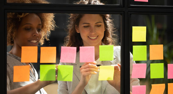 Two team members reviewing a sequence of sticky notes on a window