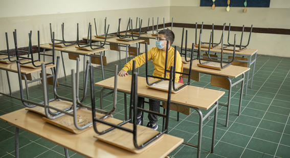 primary age student wearing mask alone in classroom of empty desks