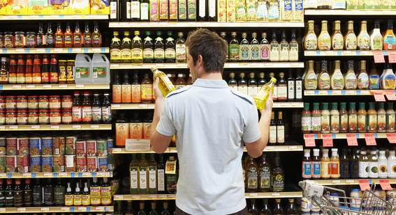 Young man in supermarket comparing bottles of oil