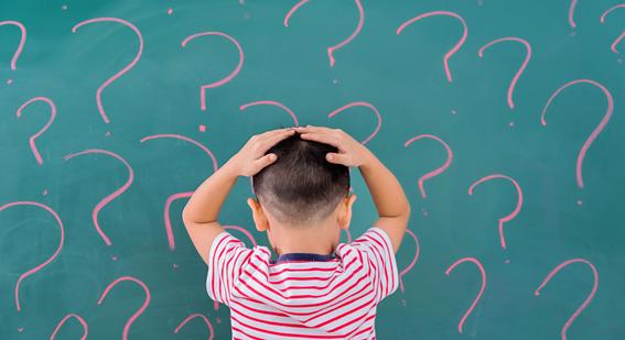 a boy with his hands on his head facing a chalk board covered in question marks