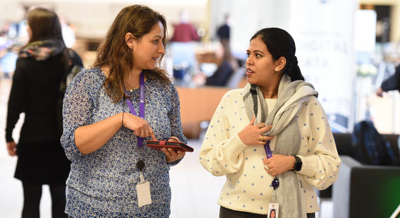 Two female colleagues look at each other in conversation while walking towards the camera