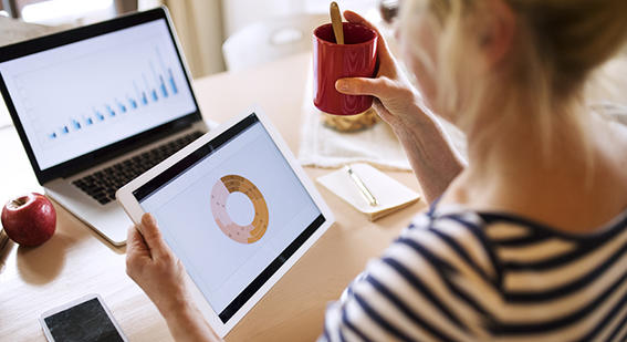 Woman looking at two different graphs on tablet and laptop screens